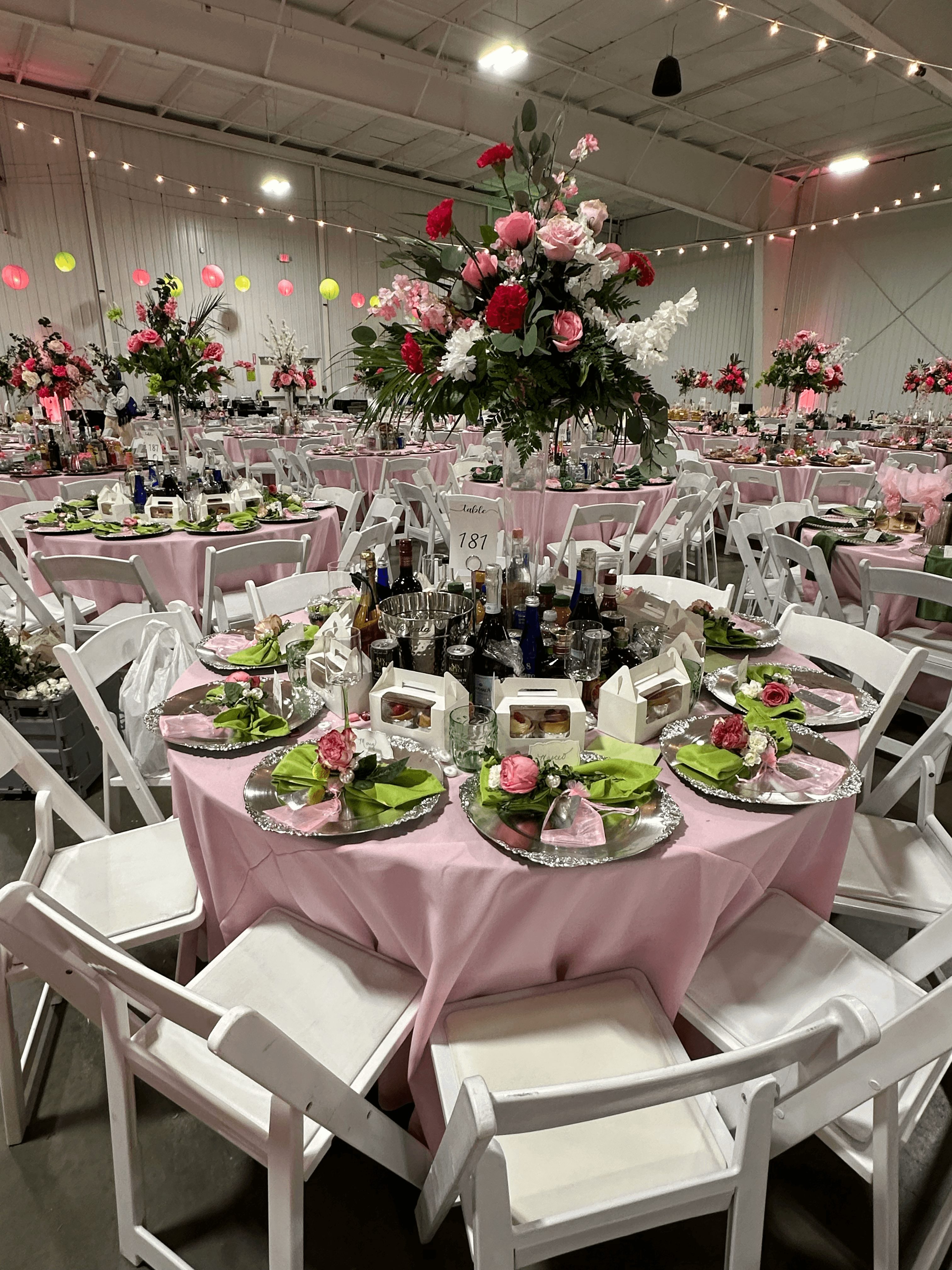 Large banquet hall with pink-clothed tables, white folding chairs, and vibrant floral centerpieces.